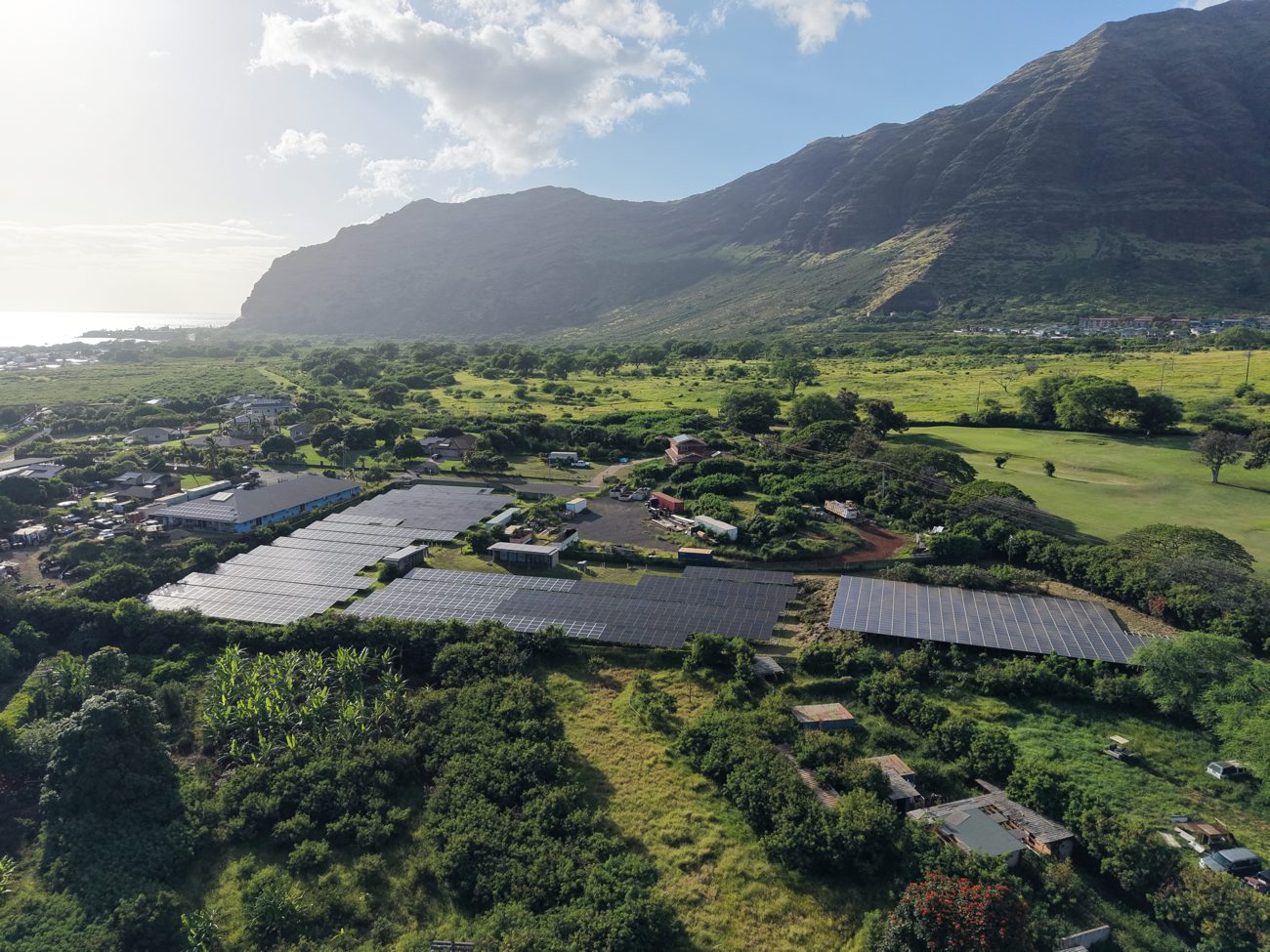 Aerial drone image of a ground-mount solar array showing terrain and access